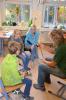 eine Frau bastelt und 2 Sch&uuml;ler und eine Frau schauen zu